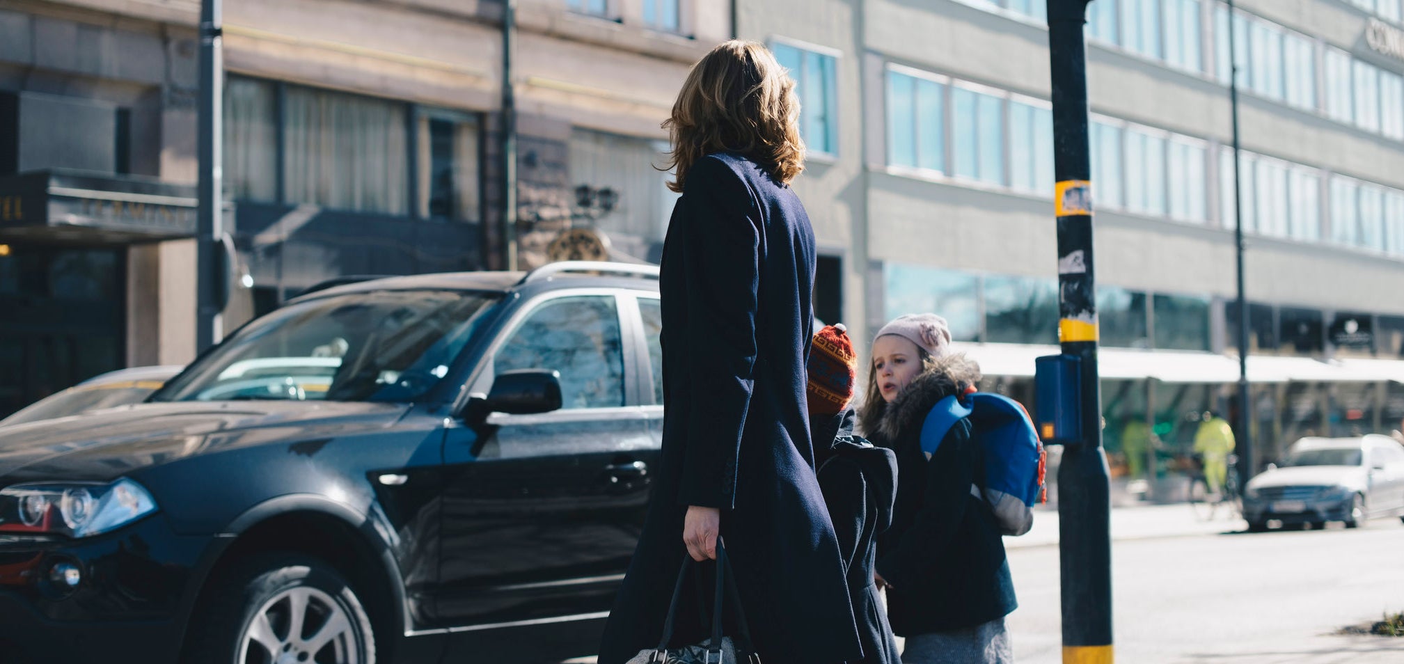 A woman with two children are crossing the street.