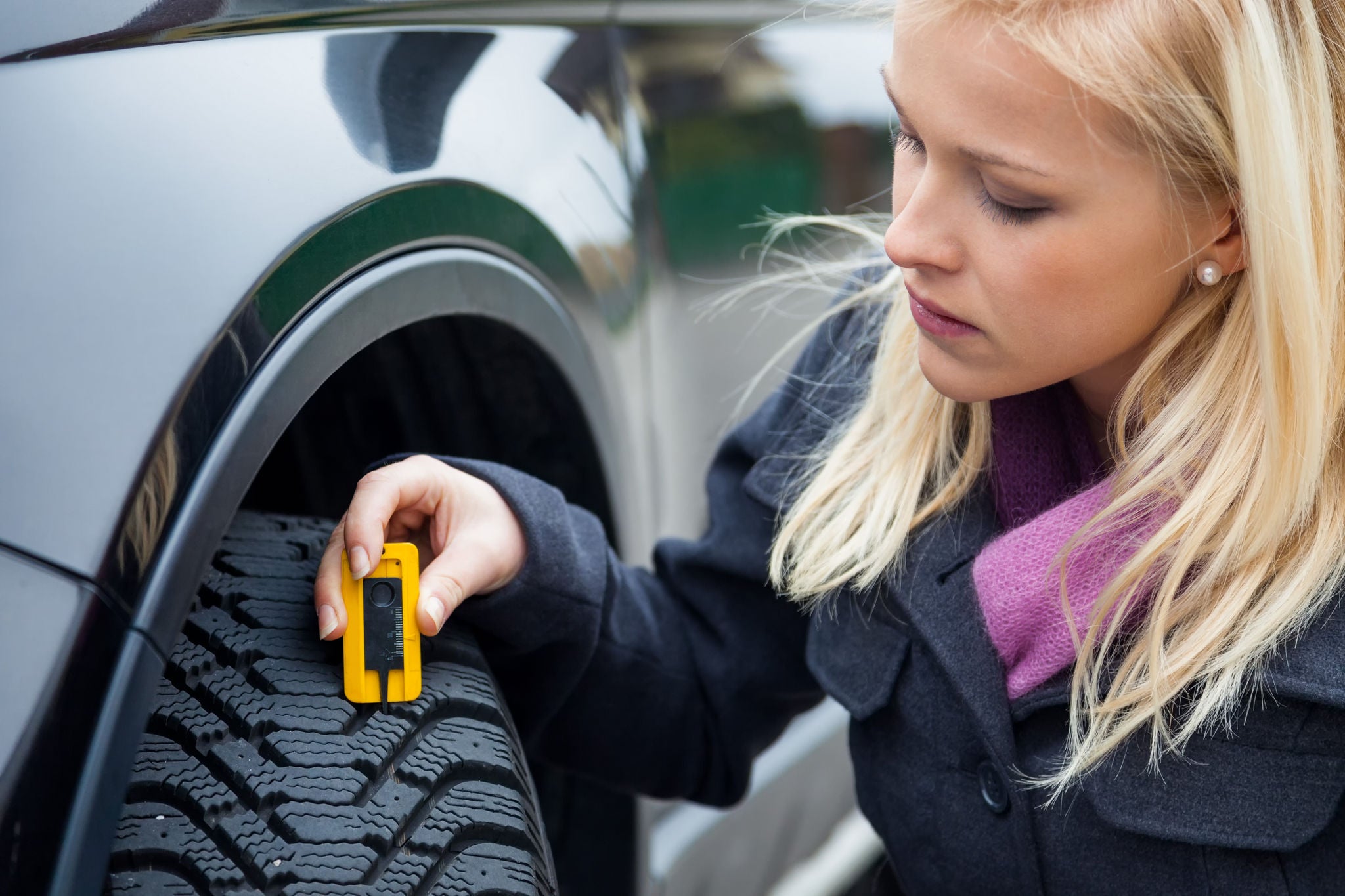 a young woman is measuring the tread depth of her car tire. the proper depth in the tread of a tire can prevent accidents.; Shutterstock ID 119524960; SAP Auftragsnummer: -; Kostenstelle: -