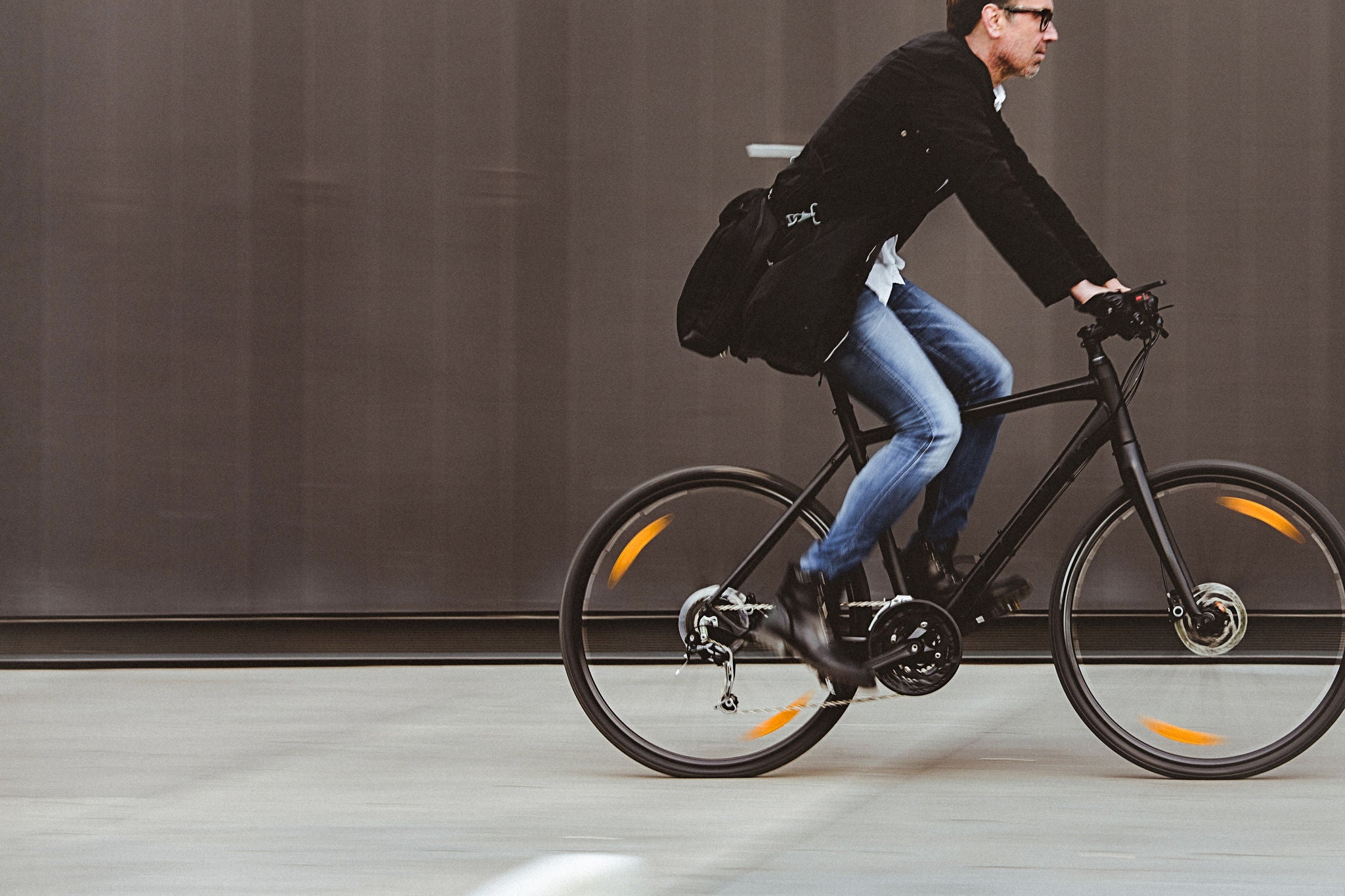 Handsome man, on the way to work, riding bicycle beside the grey wall. The man is casually dressed and wears eyeglasses and carries black briefcase hung  on shoulder. Blurred motion, copy space has been left.