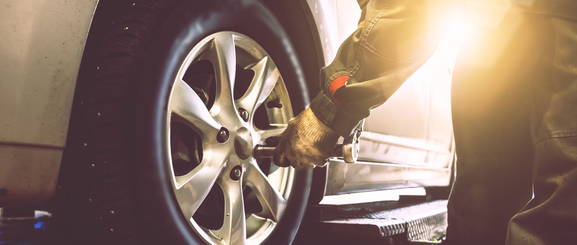 Mechanic hands with wrench changes wheel on car with special equipment in car repair service shop, sunlight effect, toned