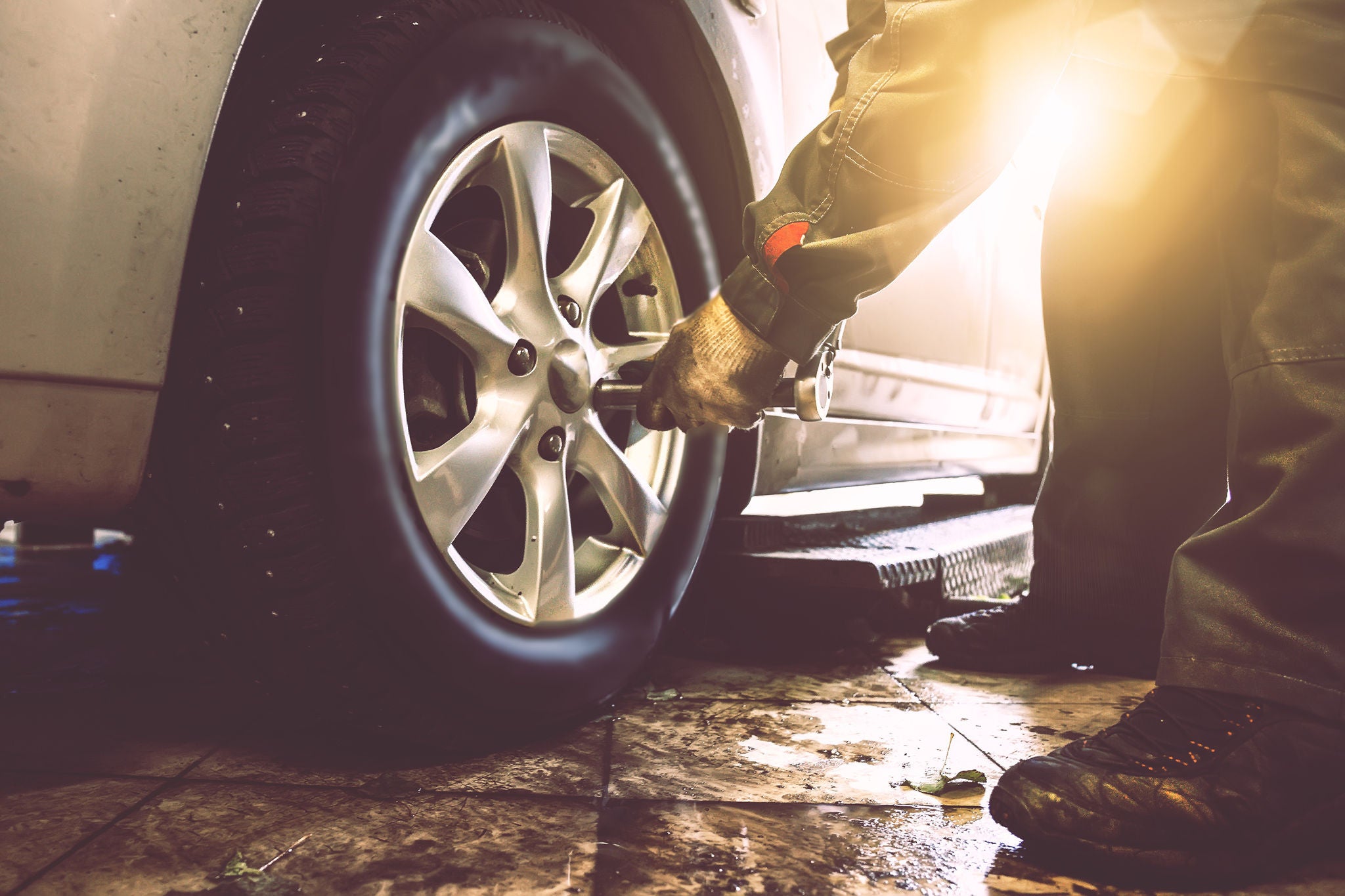 Mechanic hands with wrench changes wheel on car with special equipment in car repair service shop, sunlight effect, toned