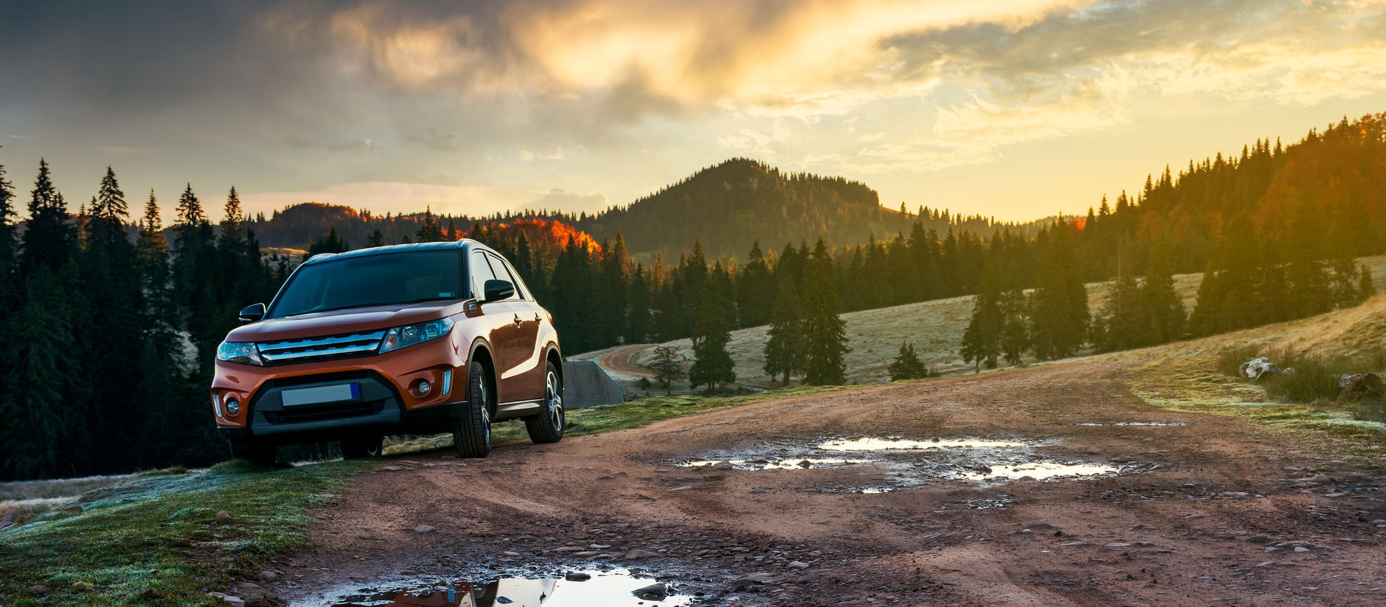 orange suv parked on the country road near forest in mountains at sunrise. beautiful autumn scenery. travel Europe by car concept